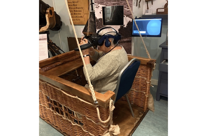 A museum volunteer tries out the Virtual Reality experience of being in a balloon basket attached to a ship in the Channel, searching for German submarines in 1917.
